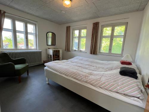 a bedroom with a bed and a chair and windows at Sejerø Vandrehjem in Sejerby