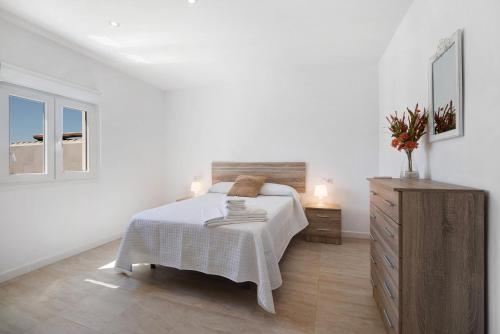 Habitación blanca con cama y tocador de madera. en Rchico Piscina climatizada 1diciemb en Chiclana de la Frontera
