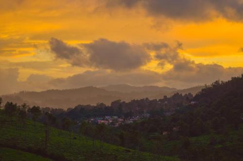 a sunset over a valley with trees and a city at Ibex Resorts, Coonoor Leewood in Coonoor