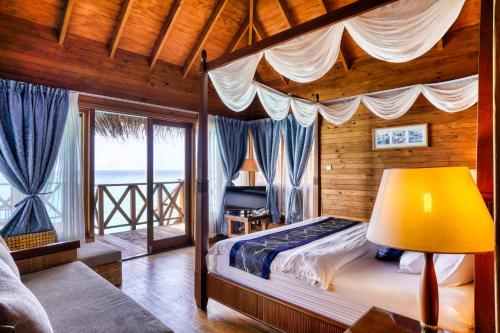 a bedroom with a canopy bed with a view of the ocean at Fihalhohi Maldives in South Male Atoll