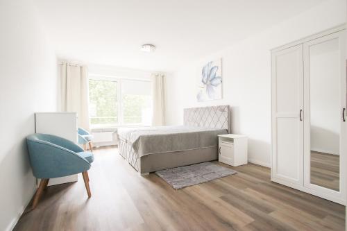 a white bedroom with a bed and a blue chair at Modernes und zentrales 4 Zimmer Apartment in Hamburg