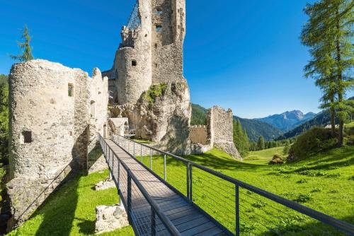 a castle on a hill with a wooden walkway at Dolomites Base Camp Hotel Olympia in Arabba