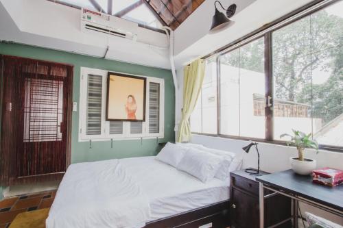 a bedroom with a bed and a desk and windows at CAMP Dakao a curated accomodation in Ho Chi Minh City