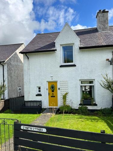 a white house with a yellow door in a yard at This must be the place - Skye, Carbost in Carbost