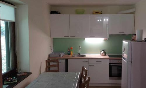 eine Küche mit weißen Schränken, einem Tisch und einem Kühlschrank in der Unterkunft Apartma Anja in Zgornje Gorje