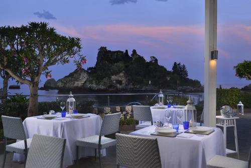 a restaurant with white tables and chairs with a view of the ocean at La Plage Resort in Taormina