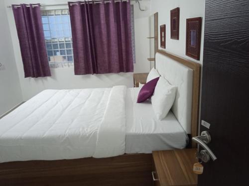 a bedroom with a large white bed with purple pillows at Purple passion in Ranipet