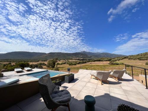 a patio with chairs and a swimming pool and mountains at Hôtel Baritedda by Le Grecale in Pianottoli-Caldarello