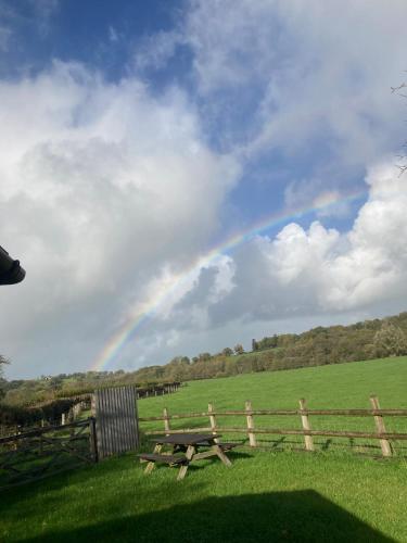 a picnic table in a field with a rainbow in the sky at Littlewood Cabin in Hatherleigh