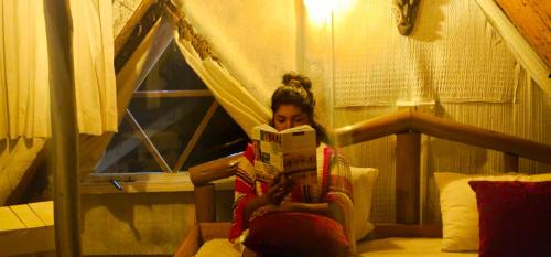 a woman sitting on a bed reading a book at haven Chalet in Nuwara Eliya
