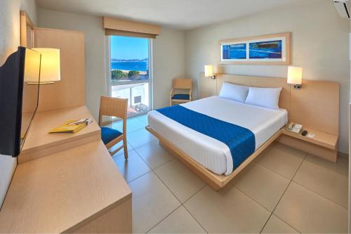 Dormitorio con cama, escritorio y TV en City Express by Marriott Manzanillo, en Manzanillo