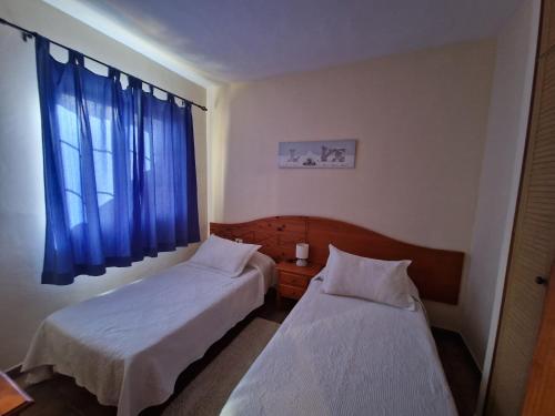 a room with two beds and a window with blue curtains at Casa Gloria in Valle Gran Rey