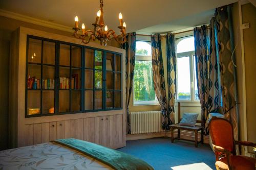 a bedroom with a bed and a chandelier and two windows at Chambre au Château de St-Pierre-Brouck in Saint-Pierre-Brouck