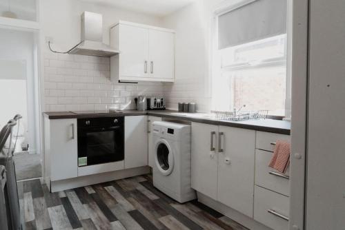 a kitchen with white cabinets and a washer and dryer at Bentley Lofts - By Sigma Stays in Crewe