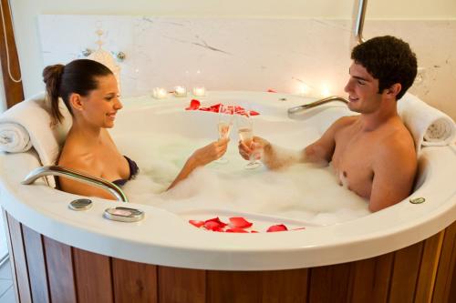 Un uomo e una donna seduti in una vasca da bagno con champagne di LS Villas Hotel & Spa ad Águas de São Pedro