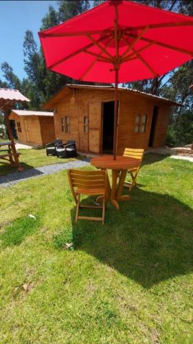 a picnic table with a red umbrella in front of a cabin at Mundo Nuevo Cabañas in Ráquira