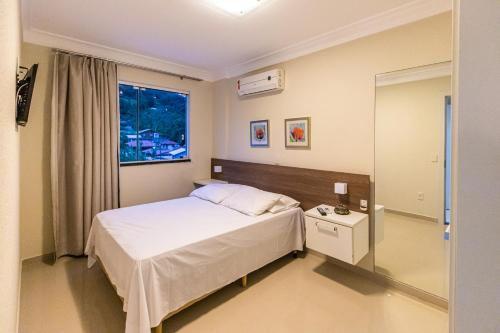 a bedroom with a white bed and a window at Flat com Piscina Térmica no Bombinhas Summer Beach in Bombinhas