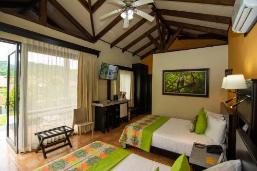 a bedroom with two beds and a desk and a window at Hotel Arenal Springs Resort & Spa in Fortuna
