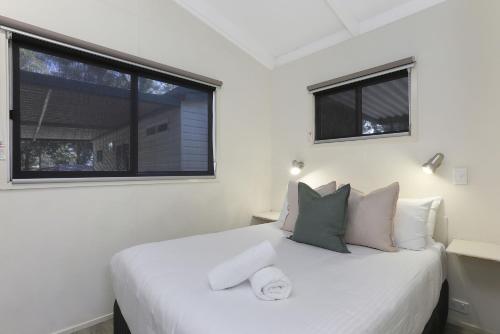 a bedroom with a white bed with two windows at Reflections Coffs Harbour - Holiday Park in Coffs Harbour