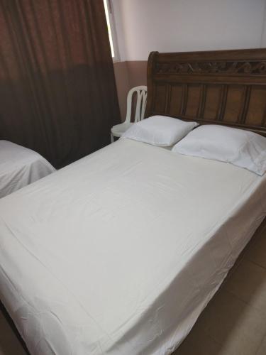 een groot wit bed met een houten hoofdeinde en witte kussens bij HOTEL MANANTIAL 1 in Playa Dormida