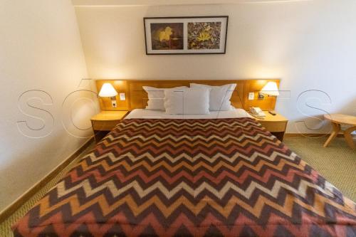 Hotel Alphaville Apto 1405 في باروري: غرفة نوم بسرير كبير مع طاولتين ومصباحين