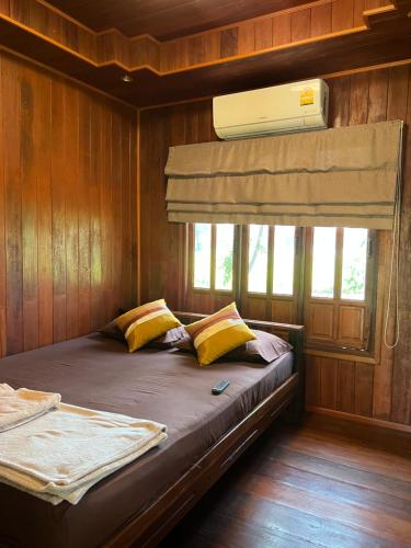 a bedroom with a bed with yellow pillows and a fan at Thakrayang Brass Artisan Home Stay in Ban Tha Krayang