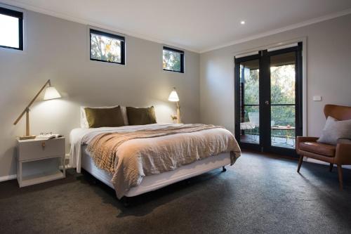 a bedroom with a bed and a chair and windows at Schafhalle in Hepburn Springs