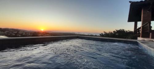 a swimming pool with the sunset in the background at 3Suítes, piscina e vista do mar em condomínio pé na areia - pátio compartilhado in Búzios
