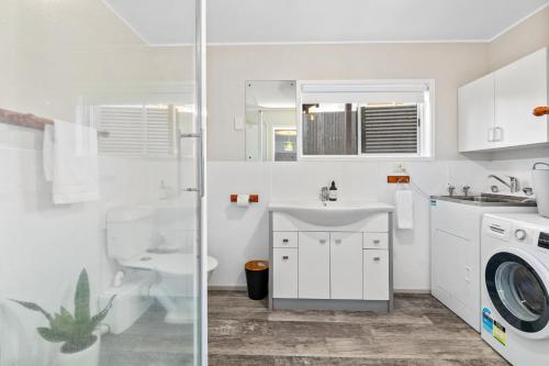 a white bathroom with a sink and a washing machine at Rooftops Rotorua in Rotorua