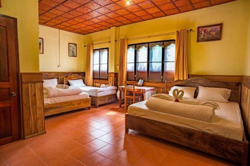 a bedroom with two beds and a table and windows at Zuela Guesthouse in Louang Namtha