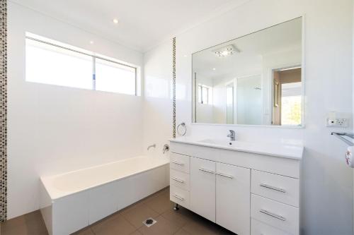 a white bathroom with a tub and a sink and a mirror at 33 Gloucester St -huge holiday house in Nelson Bay with Pool, Air Con, WiFi, Foxtel and Stunning Water Views in Nelson Bay