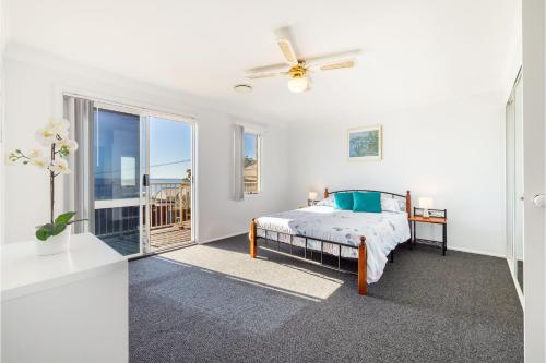 a white bedroom with a bed and a balcony at 33 Gloucester St -huge holiday house in Nelson Bay with Pool, Air Con, WiFi, Foxtel and Stunning Water Views in Nelson Bay