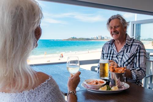 an older man and woman sitting at a table with a glass of beer at Newport Mooloolaba Apartments in Mooloolaba