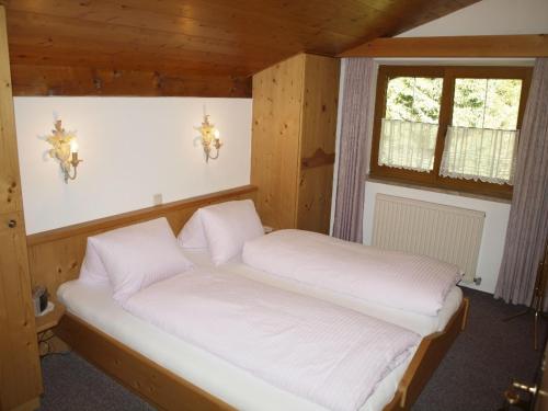 two beds in a room with wooden walls and windows at Haus Moosplatzl in Leutasch