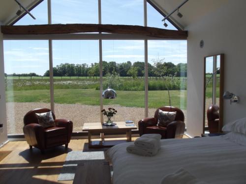 a bedroom with a bed and chairs and a large window at The Suites at Pannells Ash in Castle Hedingham