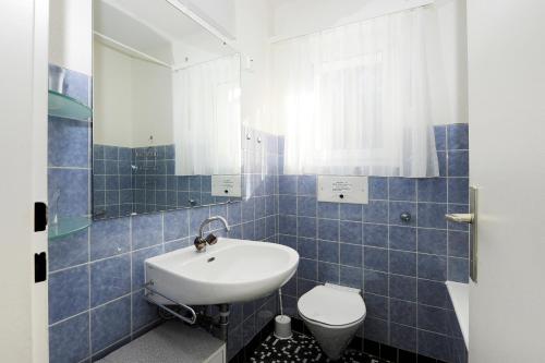 La salle de bains est pourvue de carrelage bleu, d'un lavabo et de toilettes. dans l'établissement Matterhof, à Loèche-les-Bains