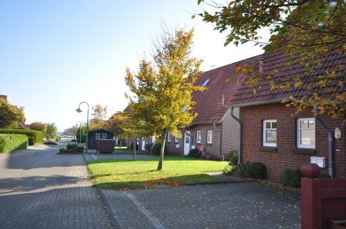 uma casa de tijolos vermelhos com uma árvore em frente em Nr 42 - Ferienhaus Im Groden Nähe Kurzentrum em Carolinensiel