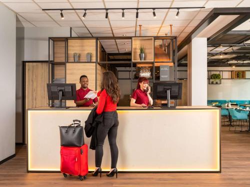 ibis Hotel Dortmund City في دورتموند: امرأة تقف في مكتب مع حقيبة حمراء