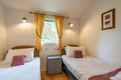 two twin beds in a room with a window at Heather Lodge 3 with Hot Tub in Belladrum