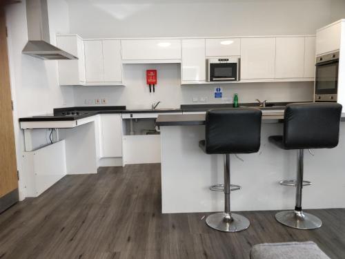 a kitchen with white cabinets and black bar stools at The Arches - The Big Yin in Stirling