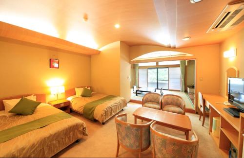 Komabaにある湯元ホテル阿智川のベッド2台、デスク、テレビが備わるホテルルームです。