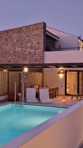 a swimming pool with white chairs and a house at RASTONI VILLAS BY AEGEAN HOUSES in Psalidi