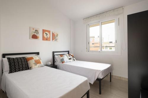 two beds in a white room with a window at Centric apartment gran via fira montjuic in Hospitalet de Llobregat