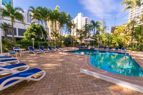 a swimming pool with blue lounge chairs and palm trees at Aegean Apartments Surfers Paradise in Gold Coast