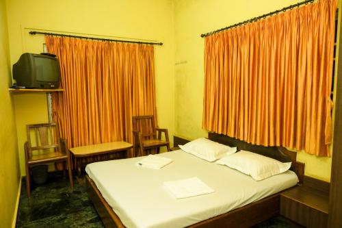 a bedroom with a bed and a tv and orange curtains at S S RESIDENCY in Padubidri