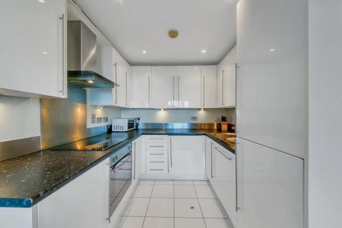 eine Küche mit weißen Schränken und schwarzen Arbeitsplatten in der Unterkunft ComfyCozy Luxury Apartment Canning Town in London