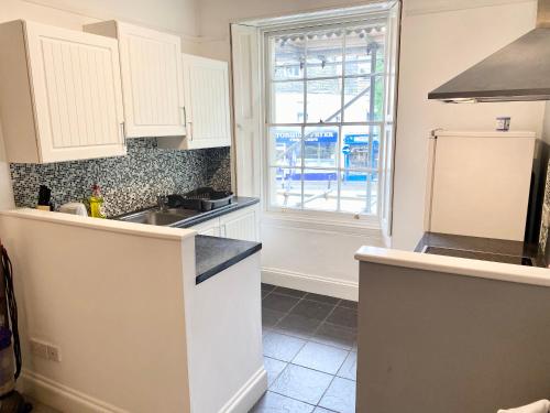 een keuken met witte kasten, een wastafel en een raam bij Remarkable 2-Bed Apartment in Torquay in Torquay