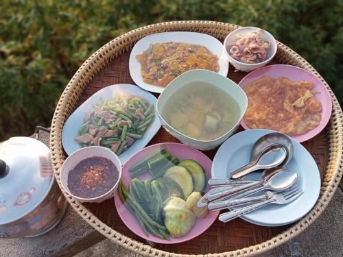 a table with plates and bowls of food and silverware at บ้านพักน้องนํ้าพุโฮมสเตย์ in Ban Yang Mae Uam