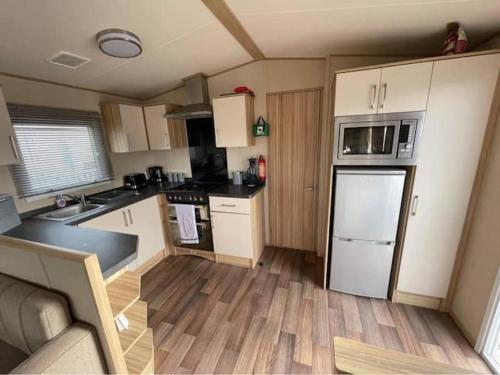 a small kitchen with white appliances and wooden floors at Beautiful 3 bed Static Caravan with Snowdon views in Caernarfon in Caernarfon