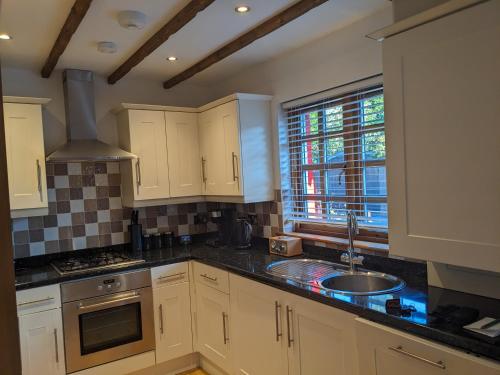a kitchen with white cabinets and a sink and a window at Heather Cottage Luss in Luss